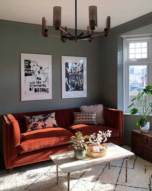 Jasny salon z czerwonym dywanem i sofą w podobnym odcieniu na tle białych ścian.