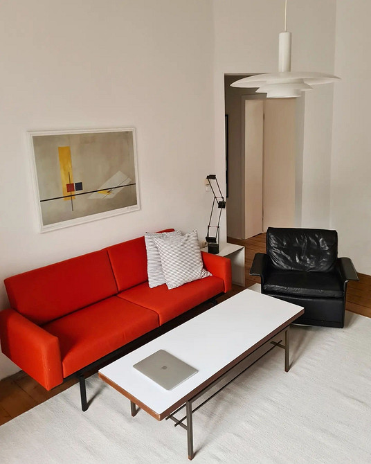 Elegancka czerwona sofa welurowa w połączeniu z białymi ścianami i złotymi akcentami