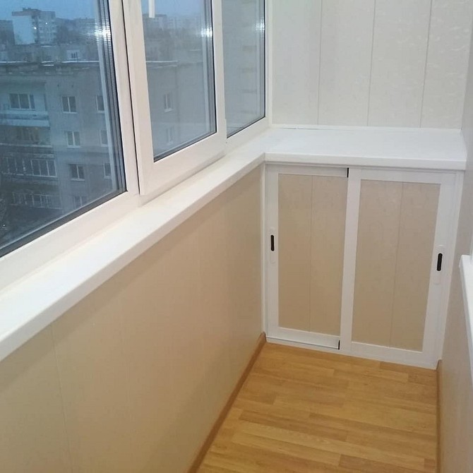 Biała szafa balkonowa Nowoczesna szafa na balkon z białymi frontami i drewnianymi półkami.