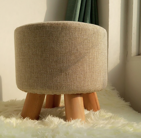 Słoneczny relaks Jasne wnętrze z pufą i fotelem blisko okna, skąpane w promieniach słonecznych.