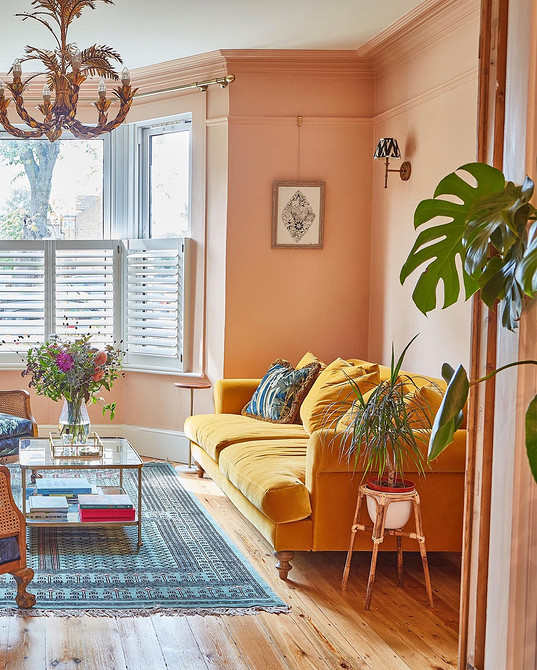 Żółta sofa z poduszkami Żółta sofa z kolorowymi poduszkami, roślinami i regałem z książkami w salonie.